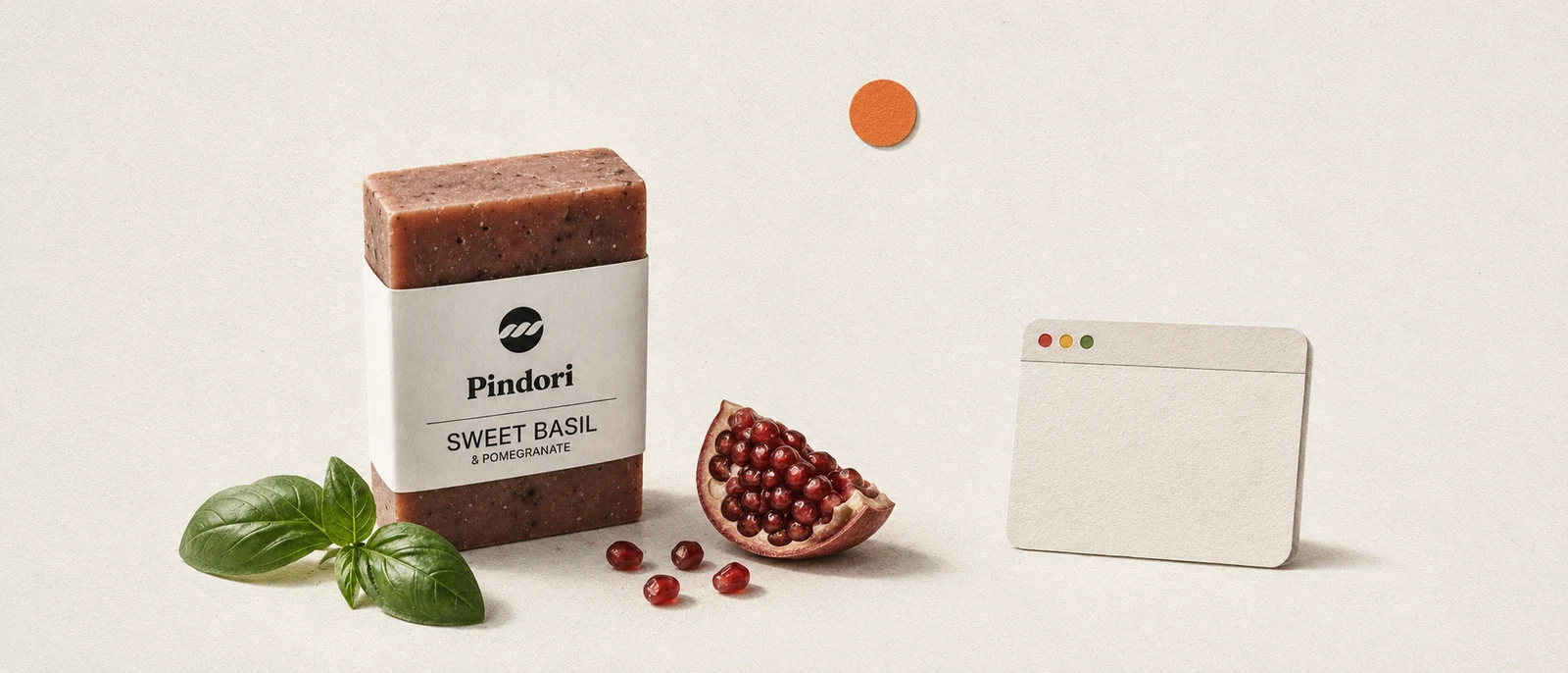 Cut-paper collage: the Pindori sweet-basil soap bar with fresh basil and a split pomegranate beside one small, mostly empty browser window.